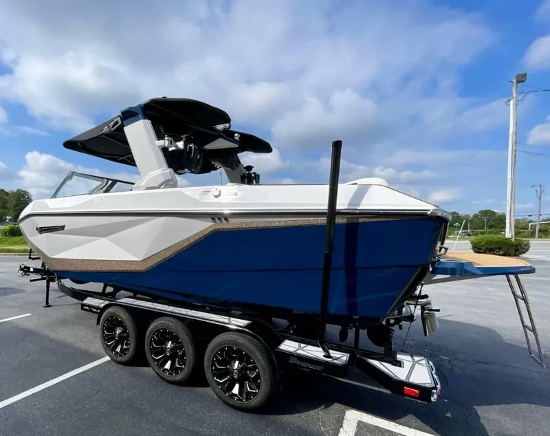 Slide: The Image of 2025 Nautique G23 boat on trailer, blue and white design, parked outdoors. - 5