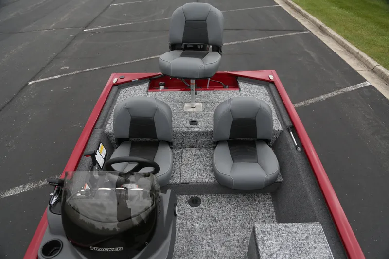 Slide: The Image of 2025 Tracker Pro 170 boat interior with gray seating and red trim, parked on asphalt. - 2