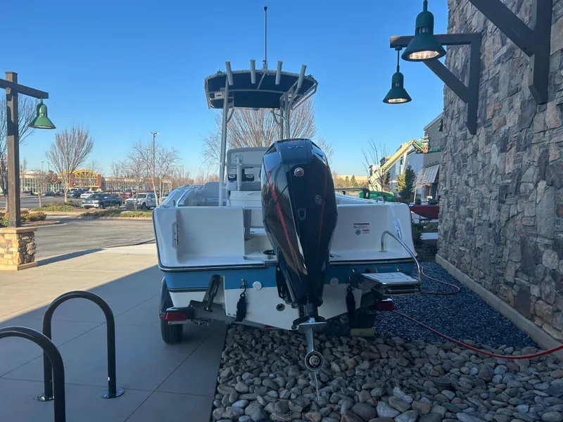 Slide: The Image of 2025 Mako 214 CC boat with outboard motor, parked outdoors on rocky surface. - 2