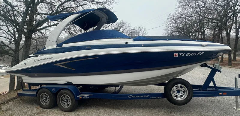 Slide: The Image of 2018 Crownline Eclipse E25 boat on trailer, blue and white design, parked outdoors. - 0