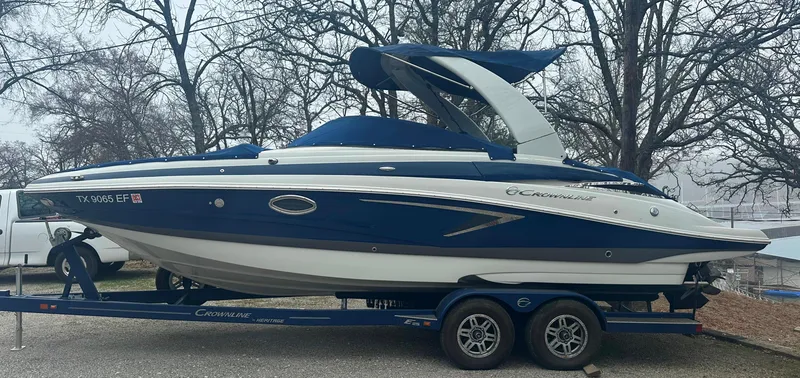 Slide: The Image of 2018 Crownline Eclipse E25 boat on trailer, blue and white design, parked outdoors. - 1
