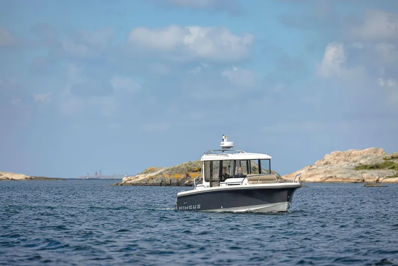 Slide: The Image of Nimbus Commuter 8 boat cruising near rocky shoreline under a clear blue sky, 2025 model. - 7
