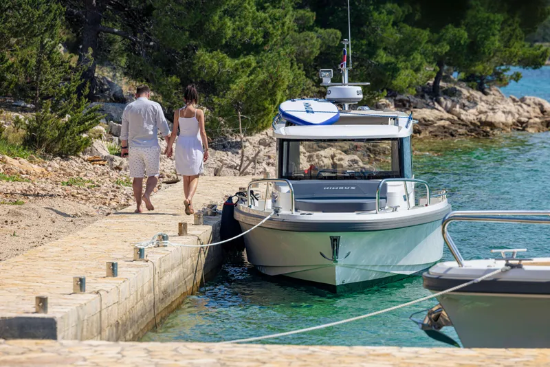 Slide: The Image of Couple walking near a 2025 Nimbus Commuter 9 boat docked by a scenic shoreline. - 14