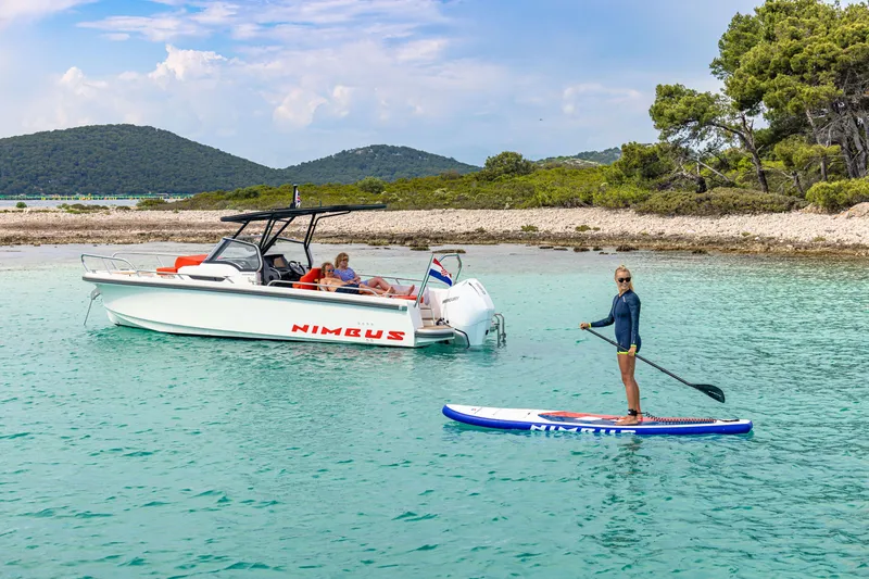 Slide: The Image of 2025 Nimbus Tender 8 boat and paddleboarder in scenic coastal waters. - 33