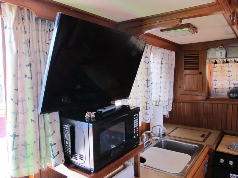 Slide: The Image of 1984 Monk 36 boat kitchen with microwave, TV, sink, and nautical-themed curtains. - 40