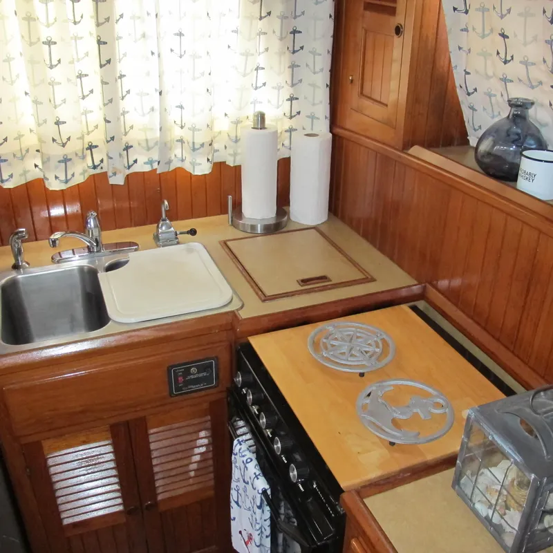 Slide: The Image of 1984 Monk 36 yacht kitchen with wooden cabinetry, dual sink, and nautical-themed curtains. - 44