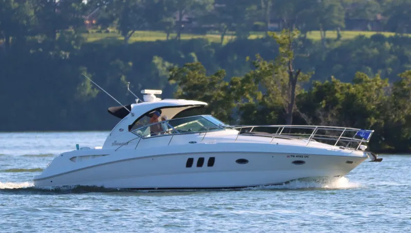 The Image of 2007 Sea Ray 38 Sundancer cruising on a scenic lake with lush greenery. - 1
