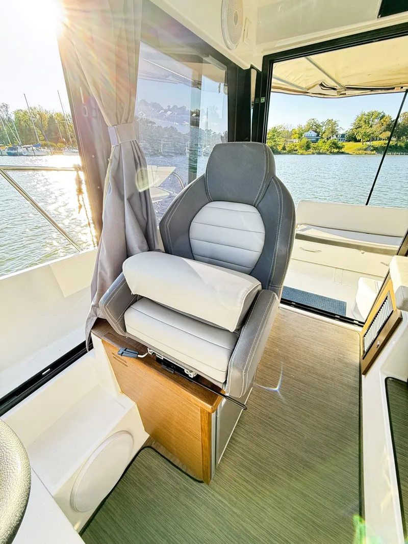 Slide: The Image of 2021 Jeanneau NC 895 boat interior with captain's chair, sunlit view, and water backdrop. - 14