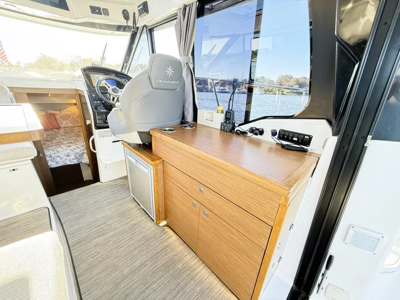 Slide: The Image of Interior of 2021 Jeanneau NC 895 boat, featuring helm, wooden cabinetry, and window view. - 19
