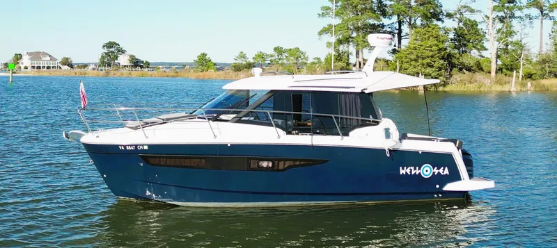 Slide: The Image of 2021 Jeanneau NC 895 boat on a serene lake with trees in the background. - 5