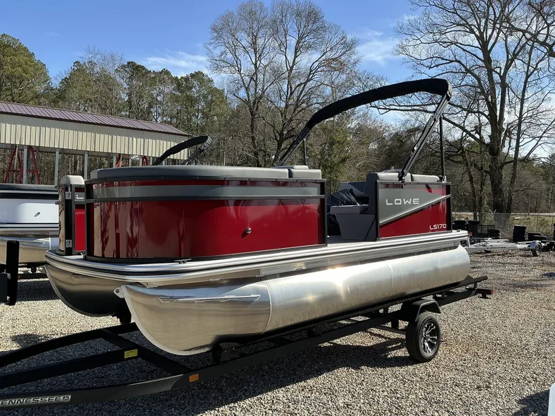 Slide: The Image of 2025 Lowe LS 170 pontoon boat on trailer, parked outdoors. - 2
