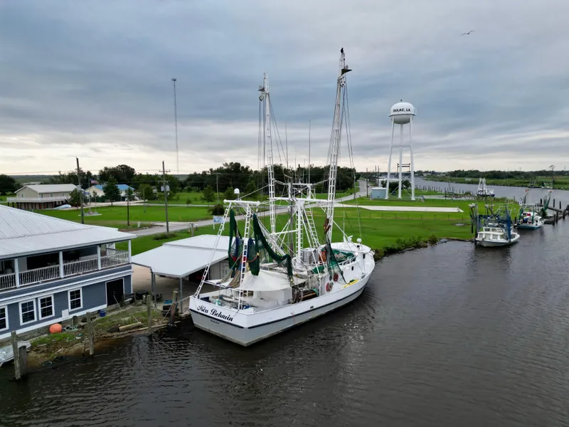 Slide: The Image of Blanchard 69 Shrimper/Freezer boat docked by riverside, overcast sky, water tower in background. - 9