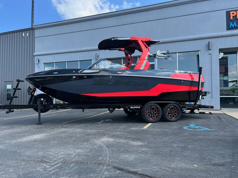 Slide: The Image of 2025 Supra SL450 boat with red and black design on a trailer outside a building. - 2