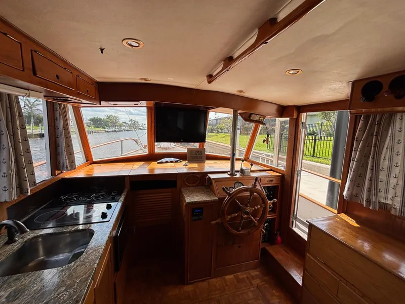 Slide: The Image of 1982 Grand Banks 36 Classic boat interior with wooden helm, kitchen, and windows overlooking water. - 18