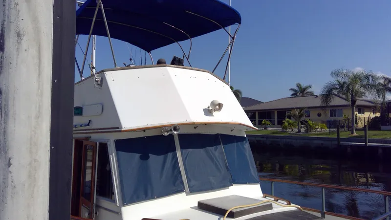 Slide: The Image of 1982 Grand Banks 36 Classic yacht docked by waterfront homes, featuring blue canopy and windows. - 4