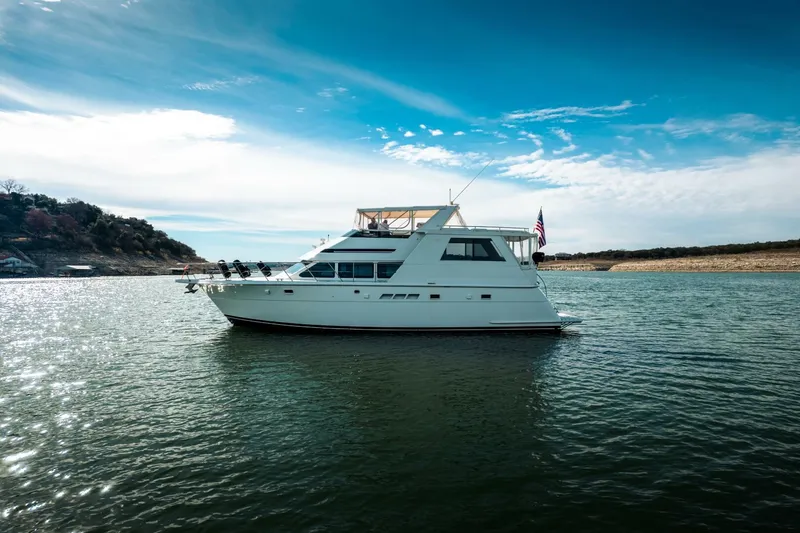 Slide: The Image of 1998 Hatteras 52 Sport Deck Motor Yacht on serene water under blue sky. - 52