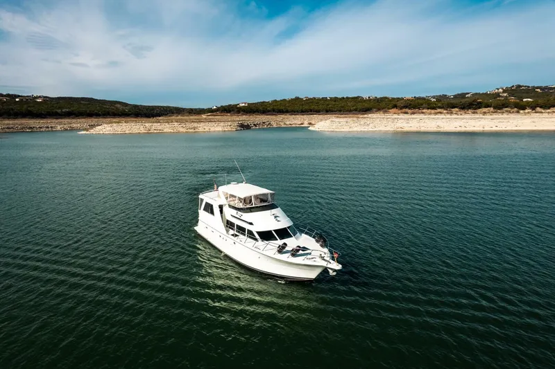 Slide: The Image of 1998 Hatteras 52 Sport Deck Motor Yacht on a serene lake under a blue sky. - 53