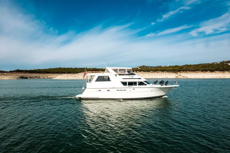 Slide: The Image of 1998 Hatteras 52 Sport Deck Motor Yacht cruising on a calm lake under a clear blue sky. - 54