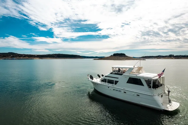 Slide: The Image of 1998 Hatteras 52 Sport Deck Motor Yacht cruising on a serene lake under a blue sky. - 63