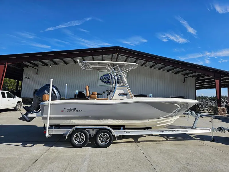 The Image of 2025 Pioneer 222 Sportfish boat on trailer, parked outside a warehouse under clear blue sky. - 1