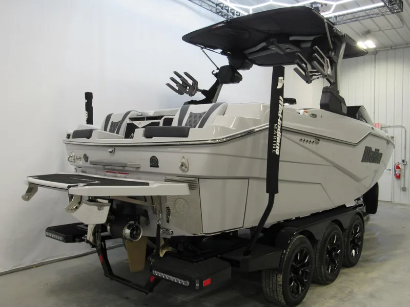 Slide: The Image of 2025 Malibu M230 boat on trailer in indoor showroom setting. - 2
