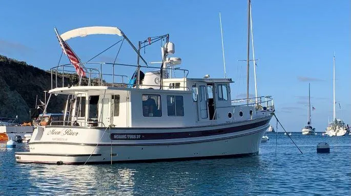 Slide: The Image of 2005 Nordic Tug 37 boat anchored in scenic harbor with clear blue sky. - 0