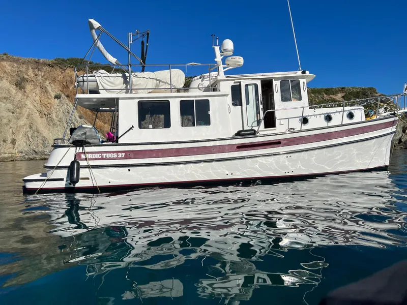 Slide: The Image of 2005 Nordic Tug 37 boat on calm water near rocky shoreline. - 1