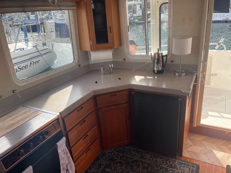Slide: The Image of Interior of 2005 Nordic Tug 37, featuring a compact kitchen with wooden cabinetry and waterfront view. - 13