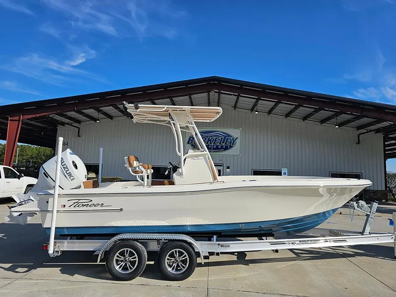 The Image of 2025 Pioneer 220 Bay Sport boat on trailer, parked outside a building under a clear blue sky. - 1