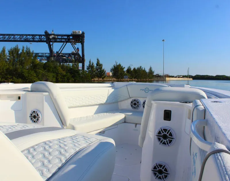 Slide: The Image of 2025 Fountain 38 SCX boat interior with white seating and speakers, near water and industrial structure. - 20