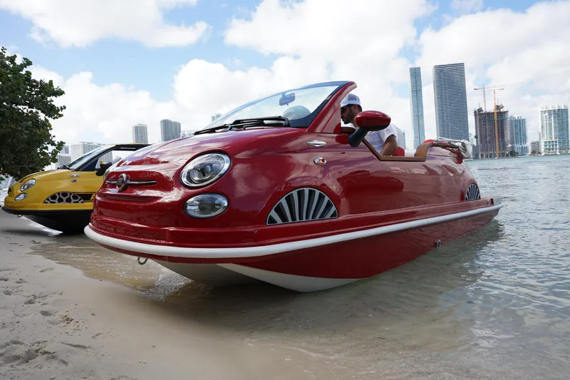 Slide: The Image of 2025 Car Off-shore Fiat 500 Classic amphibious vehicle on beach, city skyline in background. - 12