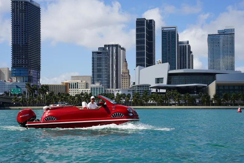 Slide: The Image of Red Car Off-shore Fiat 500 Classic boat on water, city skyline in background, 2025 model. - 13