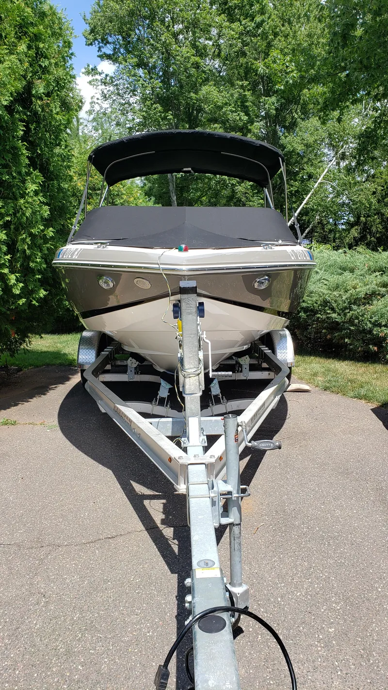 Slide: The Image of 2017 Regal 2100 boat on trailer, parked outdoors with lush greenery. - 12