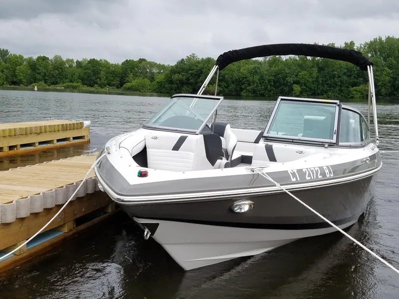 Slide: The Image of 2017 Regal 2100 boat docked on a calm lake with lush green trees. - 3