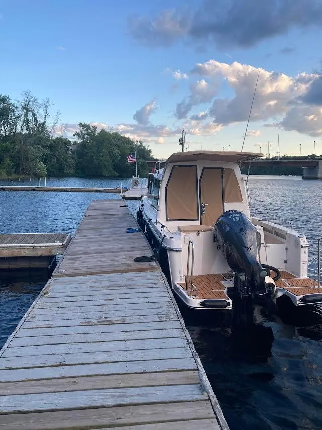 Slide: The Image of 2023 Ranger Tugs R25SC docked on a serene lake under a partly cloudy sky. - 3