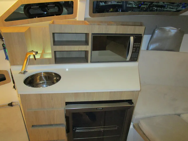 Slide: The Image of Interior of 2025 NX Boats 340 Sport Coupe featuring kitchenette with sink, microwave, and storage. - 23
