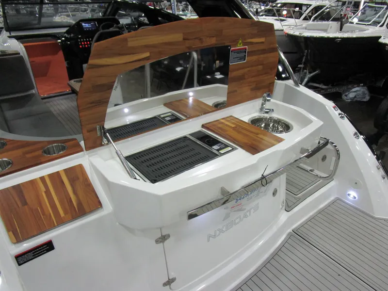 Slide: The Image of 2025 NX Boats 340 Sport Coupe with sleek outdoor kitchen and wooden accents. - 9