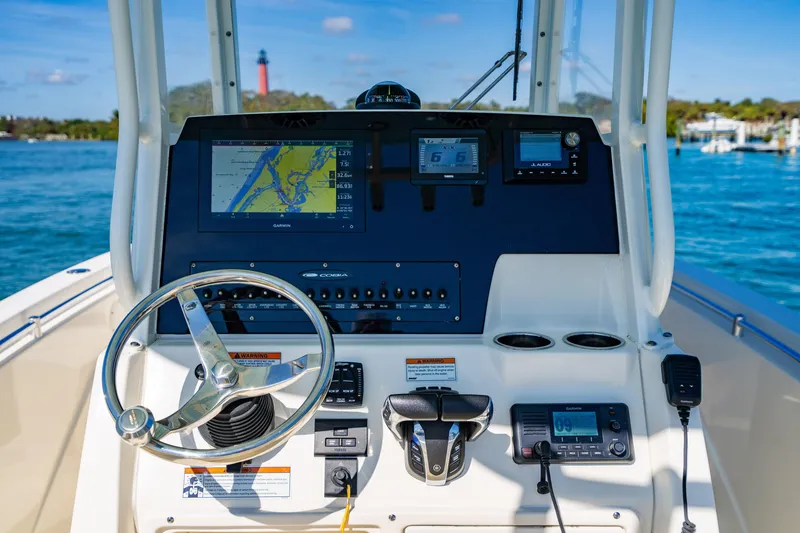Slide: The Image of 2022 Cobia 240 CC boat dashboard with navigation and control systems, steering wheel, and ocean view. - 12