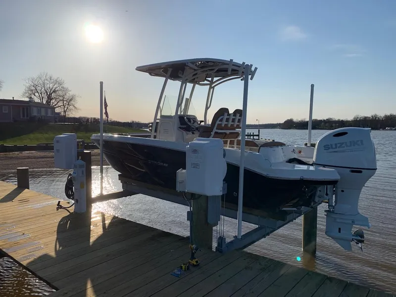 Slide: The Image of 2021 Stingray 216 CC boat on lift at sunset by the water. - 2