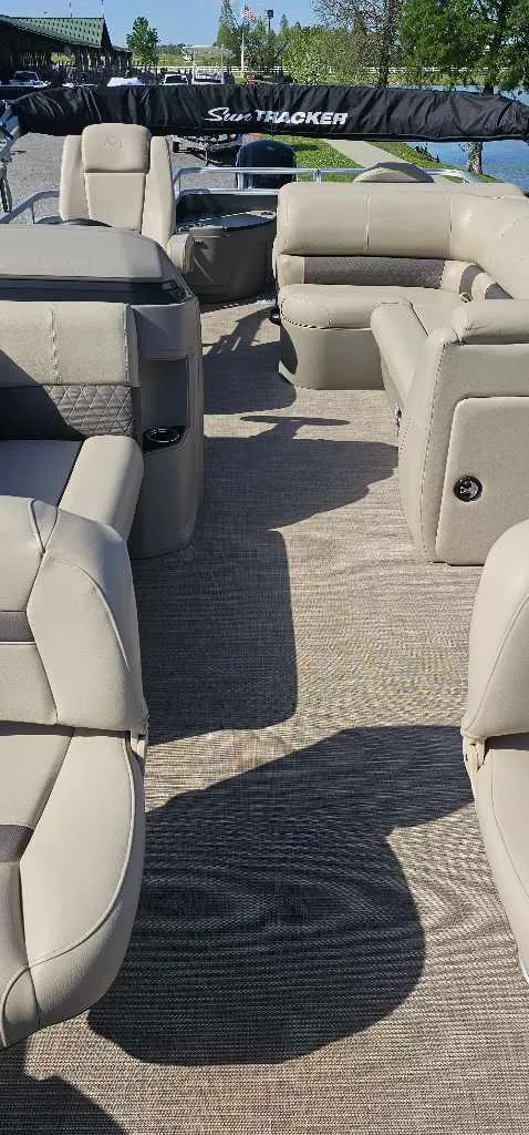 Slide: The Image of 2024 Sun Tracker Fishin' Barge 20 DLX interior with beige seating and wood-textured flooring. - 3