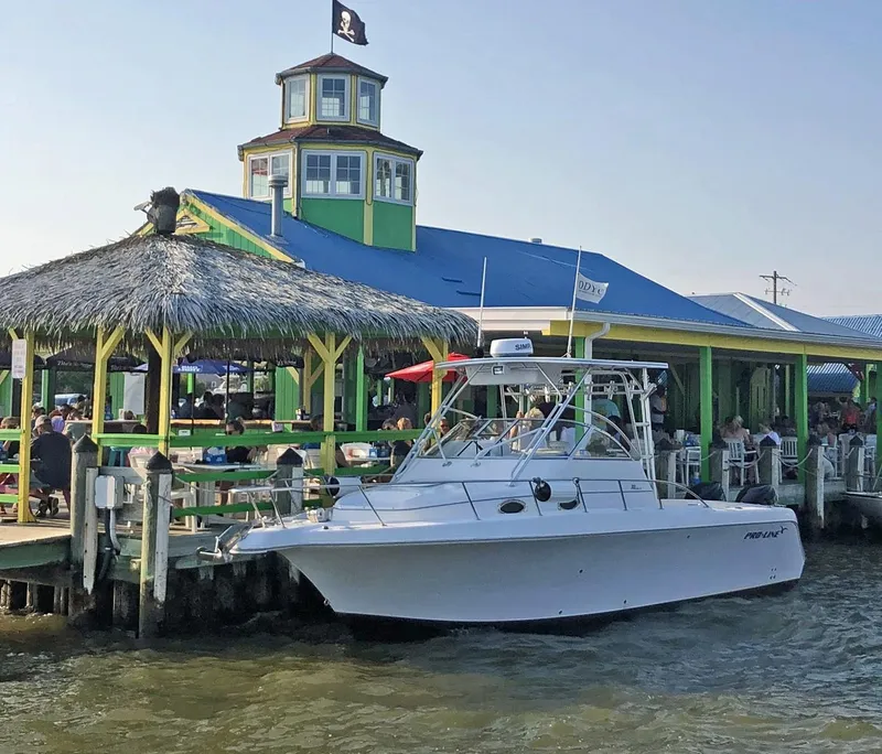 Slide: The Image of 2003 Pro-Line 30 WALKAROUND boat docked near a vibrant waterfront restaurant. - 1