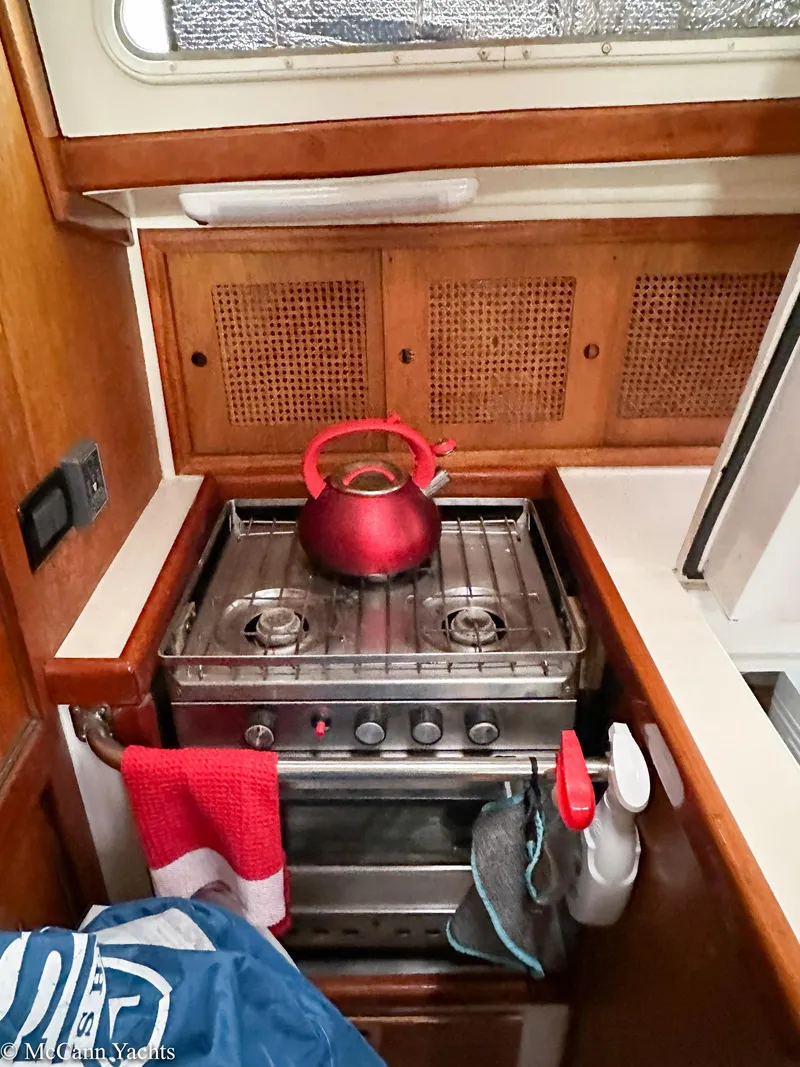 Slide: The Image of 1973 Challenger 40 yacht kitchen with stove, red kettle, and wooden cabinets. - 39