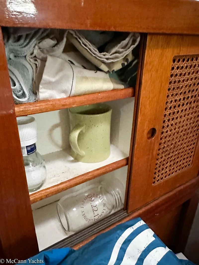 Slide: The Image of Wooden cabinet with shelves, containing a mug, bottles, and folded fabric on a 1973 Challenger 40 yacht. - 41