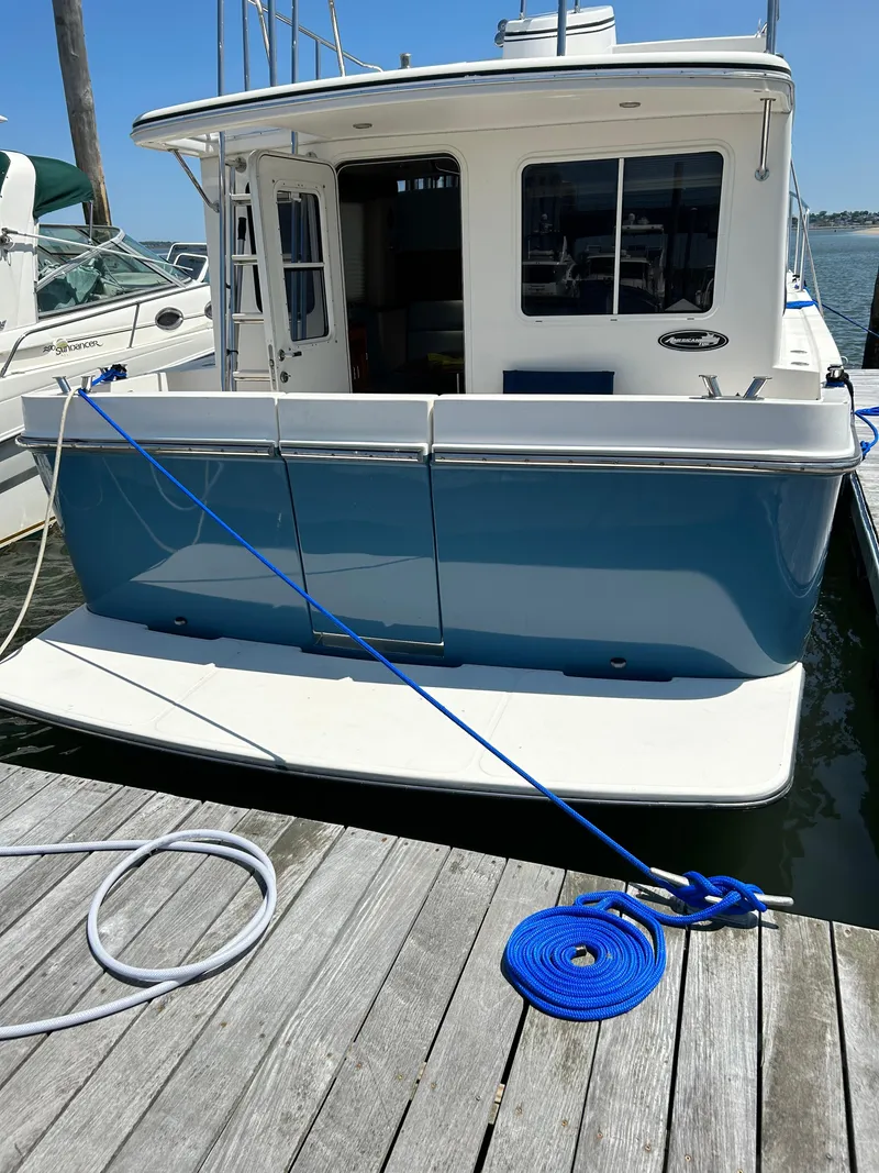 Slide: The Image of 2003 American Tug 34 docked, featuring a blue hull and white deck, secured with blue rope. - 4