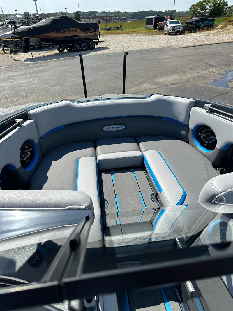 Slide: The Image of 2022 Supra SE boat interior with gray and blue seating, parked near other boats. - 12