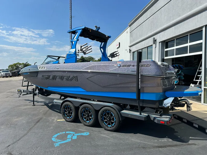 Slide: The Image of 2022 Supra SE boat on trailer, parked outside a building under a clear sky. - 2