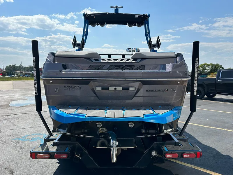 Slide: The Image of 2022 Supra SE boat rear view with wakeboard tower and blue accents in parking lot. - 3