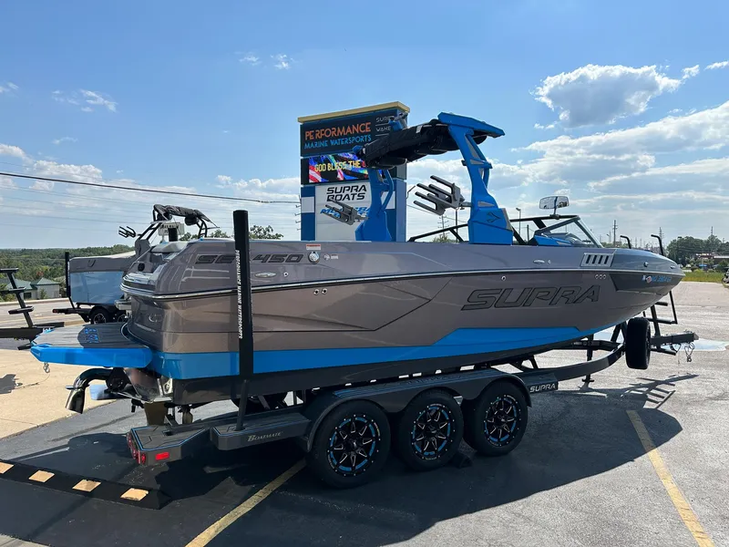 Slide: The Image of 2022 Supra SE boat on trailer, blue and gray design, parked outdoors under clear sky. - 6