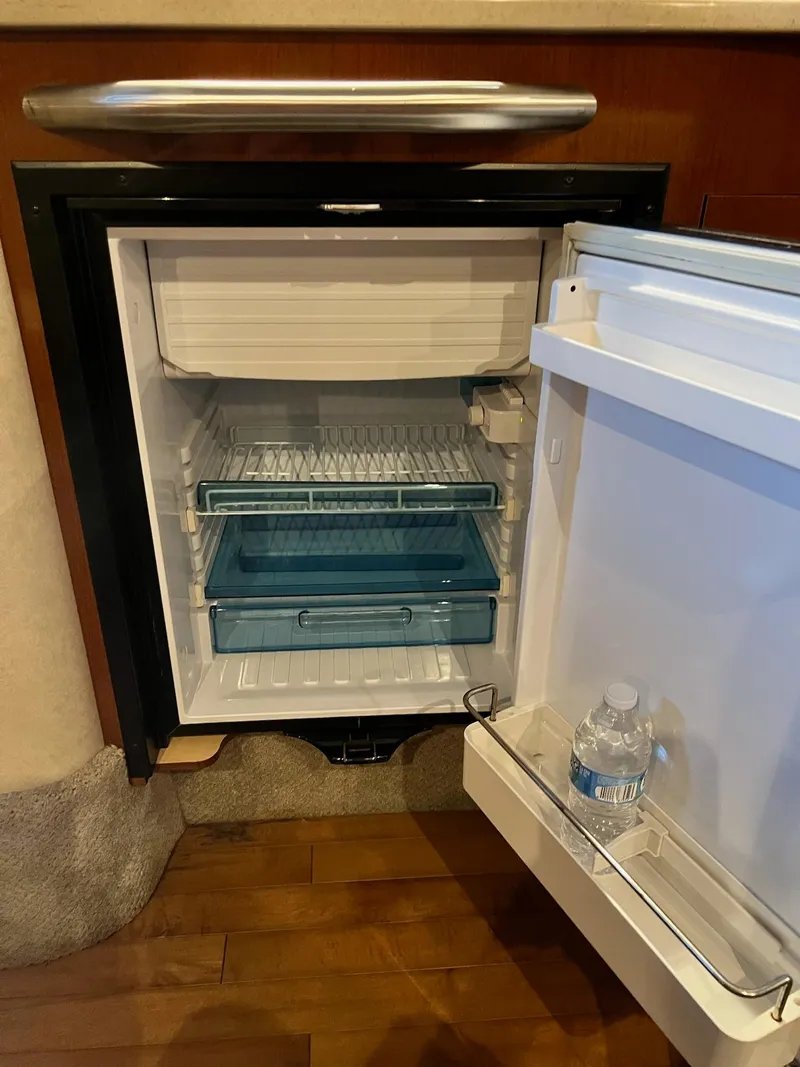 Slide: The Image of Open mini fridge inside 2011 Sea Ray 350 Sundancer yacht, with water bottle on door shelf. - 32