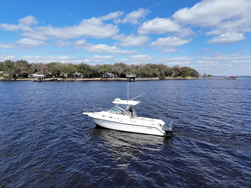 Slide: The Image of 1999 Pursuit 2870 Walkaround boat cruising on a calm lake under a blue sky. - 12